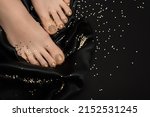 Female feet with golden nail polish pedicure. Woman legs with glitter golden nail design on black fabric background with golden paillettes