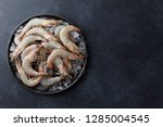 Fresh tiger prawns in a plate with ice on black textured background, top view