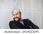 Small photo of Bearded funny man in cap of aluminum foil. Concept art phobias. Conspiracy theory. Conspiracy. Insanity.