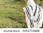 Small photo of Jew wearing tallit and Tefillin or Phylactery praying outdoors against a background of nature. Jew covers his head with tallit