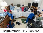 Very messy, cluttered teenage boy's bedroom with piles of clothes, music and sports equipment.  