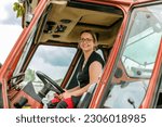Small photo of Female farmer concept: Portrait of a young blonde woman beneath a tractor in spring outdoors