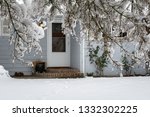 Winter view of a snow covered driveway and front of a light gray house from under a snow covered tree
