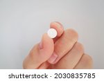 Small photo of Pill in hand. Close up to vitamin or medicine tablet between two fingers. Small round white pill. Diet supplement or drug concept holden in hand. Brigh background. Pharmaceutical product. Pain killer.