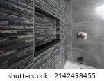 Small photo of Renovated modern bathroom with bathtub. Dark (Black Grey) tiles accent wall and niche with Grey tiles and white bathtub.