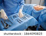 Close up of surgeon in sterile gloves getting ready medical instruments. Female patient with marks on skin lying on medical bed while doctor preparing tools. Concept of plastic surgery preparation.