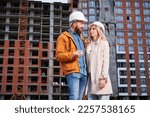Couple in safety helmets standing outside apartment building under construction. Man and woman discussing building plan outdoors at construction site.