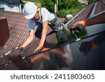 Small photo of Workers building photovoltaic solar panel system on rooftop of house. Close up of men technicians in helmets and gloves installing solar module with help of hex key outdoors. Renewable energy.