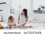 Young au pair making pancakes, cooking, baking in the white kitchen with a little girl 