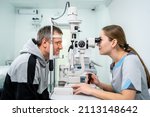 Small photo of Ophthalmologist and patient testing eyesight. Man doing eye test with optometrist. Ophthalmologist using apparatus for eye examination in clinic. Doctor examining patient doing eyesight measurement.