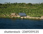 Small photo of Esna, Esna City, Esna, Luxor Governorate, Egypt - August 24th 2023 - Majestic nile energy: a large solar panel and a shack near the river banks with a man bathing in front of it.