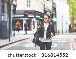 Girl walking down the street with her phone. A woman is walking alone in London. She is looking at her smart phone. Blurred on background there are  typical english houses and shops.