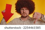 Small photo of Upset man with afro hairstyle showing red arrow pointing down, concept of downgrade, unsuccessful business, fall of stock market money exchange rate, bankruptcy fail. Hipster guy on yellow background