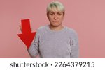 Small photo of Upset young woman showing red arrow pointing down, concept of downgrade, unsuccessful business, fall of stock market money exchange rate, bankruptcy fail. Sad girl isolated on pink studio background