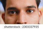 Small photo of Extreme close-up macro portrait of smiling indian man face. Young guy eyes looking at camera. Adult positive hindu man opening wide his closed eyes. Brown eyes of brunette hispanic male attractive