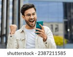 Small photo of Joyful Indian man use mobile smartphone celebrating win good message news lottery jackpot victory, giveaway online outdoors. Happy Arabian Hindu guy in downtown city street. Business people lifestyles