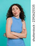 Small photo of Cheerful funny young woman showing tongue making faces at camera, fooling around, joking, aping with silly face, teasing, bullying, abuse. Girl isolated on blue studio background. Lifestyles. Vertical