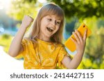 Small photo of Preteen child kid finger crossed use mobile smartphone play online game celebrating win good message news, lottery jackpot victory, giveaway. Pretty girl standing on city sunset park street, outdoors