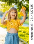 Small photo of Preteen child kid finger crossed use mobile smartphone play online game celebrating win good message news, lottery jackpot victory, giveaway. Girl standing on city sunset park street outdoor. Vertical