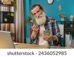 Small photo of Caucasian senior man freelancer counting cash insufficient amount of money. Financial crisis. Bankruptcy. Poverty and destitution. Sad upset grandpa with laptop netbook sitting at home office table.