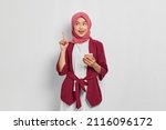 Small photo of Excited beautiful Asian woman in casual shirt and hijab holding mobile phone and pointing finger up, creating genius solutions isolated over white background. People religious lifestyle concept