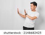 Small photo of Portrait of serious young Asian man showing stop gesture, demonstrating denial sign, rejecting something unwanted isolated on white background