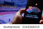 Small photo of Jakarta, Indonesia - May 31, 2022: The 19th Asian Games Hangzhou 2022 logo displayed on smartphone with inside stadion background. This event was postponed to 2023 due to the COVID-19 case in China