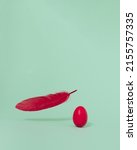 Small photo of Bold red Easter egg with feather next to it on pastel green background with copy space. Minimal concept of circle of life. Idea of easier or harder heavier things.