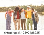 Small photo of A diverse group of friends shares a moment of closeness by the lake, their body language suggesting comfort and familiarity with one another. The central figure stands out with a bright yellow shirt