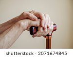 Small photo of Macro shot of elderly woman's hands holding the wooden handle of a metal walking cane. Close up, copy space for text, neutral background.