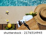 Small photo of Swimming pool essentials concept. Beach bag with items for safe sunbathing on the deck, sunglasses, straw hat, white blanket and sunscreen product. Copy space, top view, background.