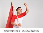 Excited young Asian man standing holding Indonesian flag with raised hands while Celebrate Indonesia independence day on 17 August isolated over white background