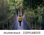 Small photo of Close view of a woman with a yellow anorak walking on the suspension bridge with metal fence over the Mino river in Spain in an environment of native trees.