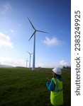 Small photo of A female operator looks at a wind turbine and holds a notebook in her hands while writing the dossier, with space for copy. Rural renewable energy area.