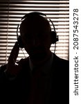 Small photo of Silhouette of an FBI secret agent, listening with headphones and recording the conversation against the backdrop of a window with blinds, silhouette lighting, selective focus, dark tonality.