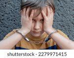 Small photo of A juvenile delinquent in handcuffs against a gray wall, close-up. Concept: juvenile delinquency, petty theft and theft, incarceration.