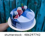 Hand holding ombre marble mousse cake decorated with blue and violet mirror glaze, fruits and macaron. Modern dessert. Wooden hand painted blue background.