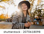attractive young woman walking in autumn street wearing checkered coat, black hat, happy mood, fashion style trend, black friday sale, sunny