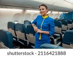 Small photo of Joyful woman stewardess in airline air hostess uniform looking at camera and smiling while resting hand on passenger seat