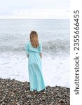 Small photo of a slender girl in a blue dress stands on the seashore with her back and looks beyond the horizon, waiting for poetry poetry muse