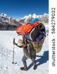 Small photo of Nepalese Sherpa Porter walking on Glacier with trekking Pole carrying Basket with lots of Mountain Expedition Luggage using traditional Head Strap in Himalaya