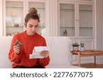 Small photo of Focused woman examining drug package leaflet for prescribed medicine while sitting at home holding bluster of capsules