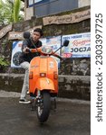 Small photo of Yogyakarta, Indonesia - Dec 31 2022: A man poses with his bright orange vespa strada aom motorcycle in a village parking space. Translate: mbayung green lombok stall benny, skilled in jogja