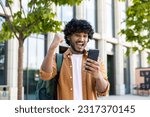 Young hispanic student celebrating victory and happy good news online, man reading page interent received notification and message, hold phone, use app win and good achievement.
