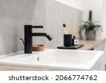 An elegant black bathroom faucet and white square sink with a blurry cup, toothbrushes and plant