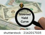 Inverted Yield Curve.Magnifying glass showing the words.Background of banknotes and coins.basic concepts of finance.Business theme.Financial terms.