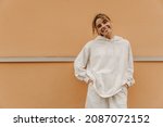 Beautiful caucasian young girl smiling with teeth looking at camera on background with place for text. Swarthy blonde beauty wears white warm tracksuit. Good mood, fashion trends