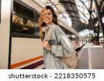 Small photo of Happy young caucasian woman smiles with teeth looking at camera going on train trip. Blonde wears denim jacket, backpack. Spring break concept.