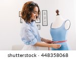 A brunette girl in a blue shirt is working in the workshop studio. She makes fitting on the blue dress on the  mannequin.