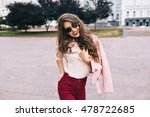 Portrait of cute girl with long curly hair and phone in hands smiling to camera in city on bulding background.